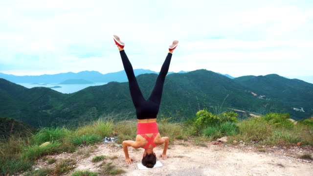 Young-woman-practicing-yoga-headstand-on-top-of-rock.-Landscape-mountain-view.