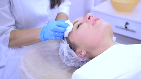 Beautician-cleans-female's-face-skin-in-beauty-clinic