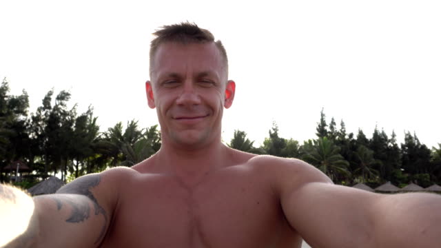 Man-taking-selfie-using-phone-on-beach-smiling,-enjoying-vacation