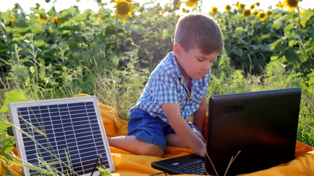 tecnología-de-generación-de-energía,-feliz-niño-con-ordenador-portátil-alimentado-por-batería-solar-en-el-campo-de-fondo-de-girasoles