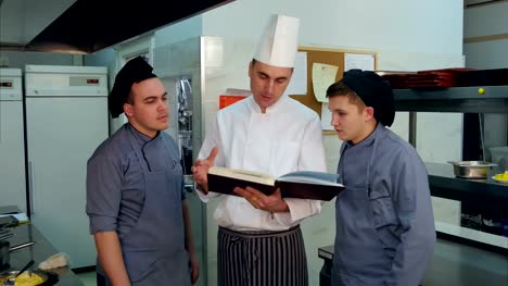 Jefe-de-cocina-sosteniendo-el-libro-de-recetas-y-hablar-de-algo-con-sus-aprendices