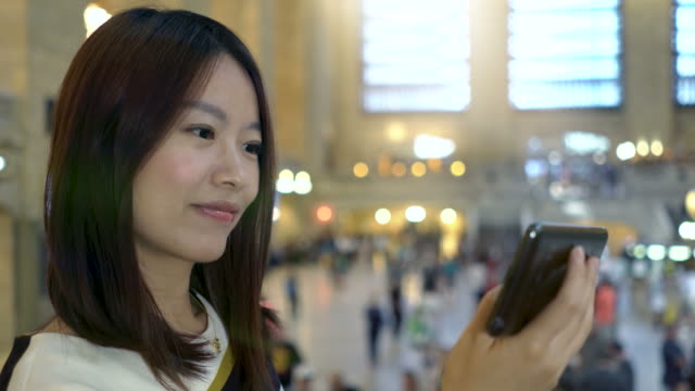 Mujer-asiática-atractiva-usando-el-teléfono-en-la-ciudad.-Ojos-oscuros-y-cabello-oscuro.-Fondo-lleno-de-gente-y-urbano.