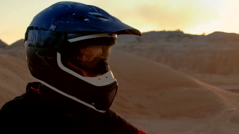Close-up-Portrait-Shot-Of-the-Extreme-Motocross-Rider-in-a-Cool-Protective-Helmet-Standing-on-the-Off-Road-Terrain-He's-About-to-Overcome.-Background-is-Sandy-Track.
