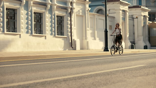 Bicicleta-de-mujer-de-cabello-rojo-del-montar-a-caballo-en-la-calle-de-la-ciudad-en-el-edificio-de-fondo