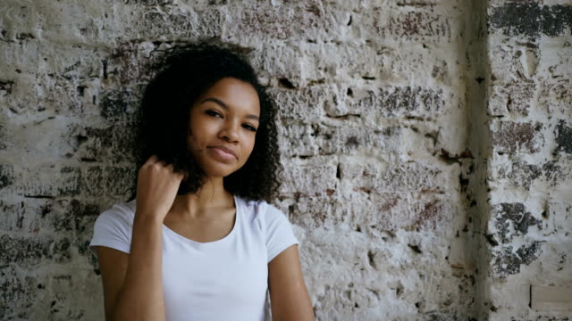 Portrait-of-young-smiling-mixed-race-woman-flirting-and-looking-into-camera-on-brick-wall-background
