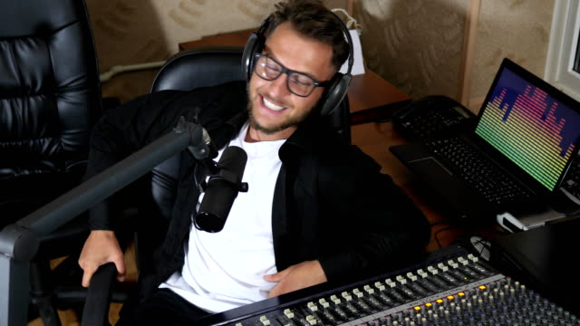 radio-presenter-in-glasses-speaks-into-microphone-beside-mixing-console
