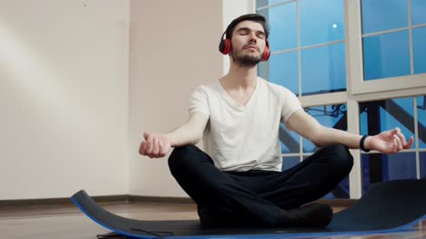 Junger-Kerl-meditieren-auf-Boden-und-hören-Musik-im-Kopfhörer
