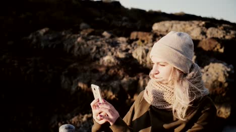 Retrato-de-joven-rubia-de-pie-en-las-montañas-en-día-soleado-y-tomar-foto-selfie-en-smartphone
