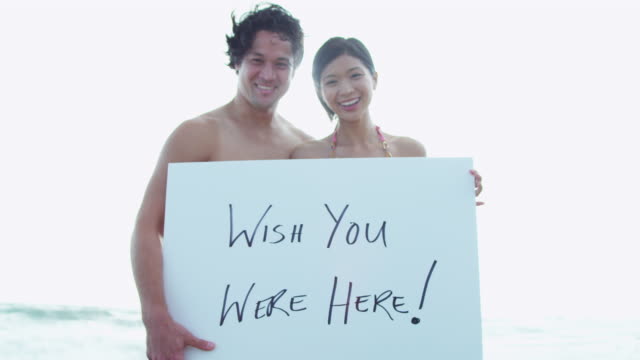 Feliz-pareja-étnica-viendo-saludos-vacaciones-tablero-blanco