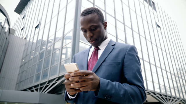 young-afro-american-businessman-in-the-street-types-on-his-smartphone