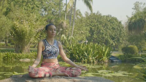 Young-asian-woman-doing-yoga-outside-in-the-park.-Attractive-woman-meditate-in-lotus-pose-in-beautiful-sun-light.