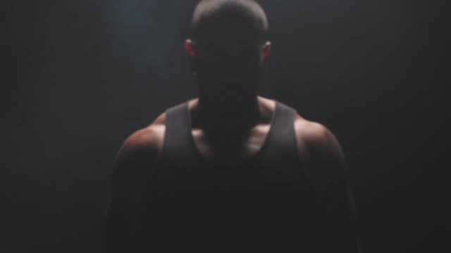 Portrait-shot-of-a-muscular-black-man-staring-at-the-camera-on-a-foggy-dark-background.