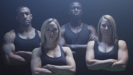 Group-of-athletes-staring-at-the-camera-with-their-arms-crossed-on-a-foggy-dark-background