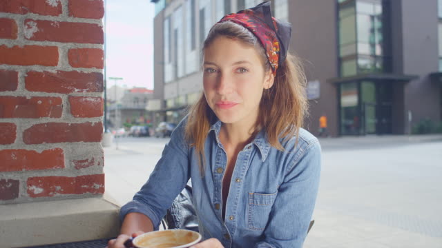Mujer-joven-inconformista-sentado-afuera-de-una-tienda-de-café-sonríe-y-bebe-su-café,-retrato