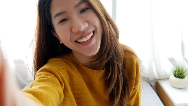 Schöne-asiatische-Frau-unter-Selfies-auf-einem-Smartphone-im-Schlafzimmer-zu-Hause.