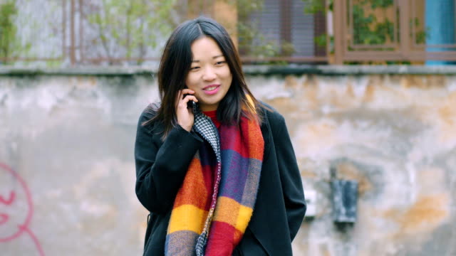 Smiling-relaxed-asian-woman-talking-by-phone--outdoor