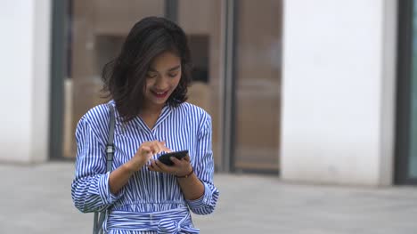 Mujer-asiática-joven-usando-el-teléfono-inteligente-en-la-calle