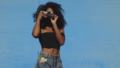 Schöne-junge-Frau-Fotografieren-mit-Film-Kamera-an-bunten-blauen-Wand