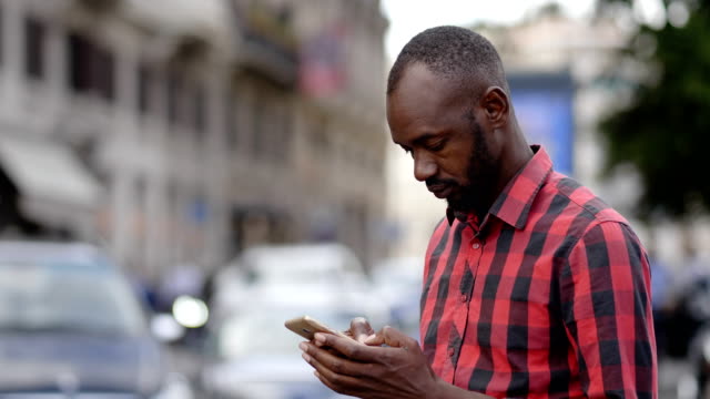 hübscher-junger-schwarzer-Mann-mit-Smartphone-auf-der-Straße