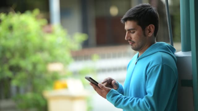 Young-happy-Persian-man-using-phone-outdoors