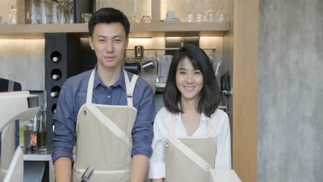 Portrait-of-two-young-asian-barista-man-and-woman-crossing-hands-and-smiling-on-the-camera-in-the-coffee-cafe