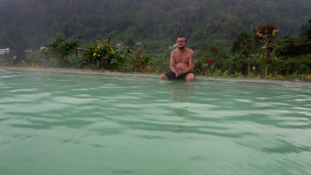 Un-hombre-se-sienta-en-el-borde-de-una-piscina-con-agua-termal-caliente