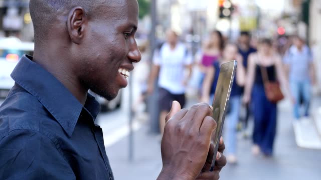 Smiling-attractive-young-balck-man-using-tablet-in-the-street--slow-motion
