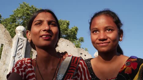 Zwei-Frauen-kleben-sprechen-gemeinsame-Sitzung-starrte-in-gleichen-Ort-Seitenprofil-auf-einer-Terrasse-in-traditioneller-Kleidung-in-Indien-handheld-zwei-mittlere-Schuss-Liebe-Tradition-ländlichen-outdoor-Sommer-Hitze-Sonne