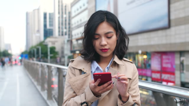 Eine-hübsche-junge-Asiatin-mit-Handy-in-der-Stadt