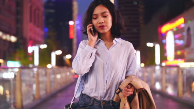 Slow-Motion-ziemlich-glücklich-junge-asiatische-Frau,-die-zu-Fuß-in-die-Stadt-Straße-während-des-Gesprächs-am-Telefon-am-Abend