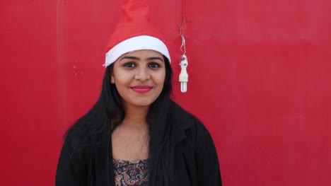 Junge-indische-Frau-mit-Santas-Hut-willkommen-und-machen-Handgesten,-aufgeregt-und-super-glücklich,-mit-einem-passenden-roten-Hintergrund,-handheld-Gimbal-stabilisiert