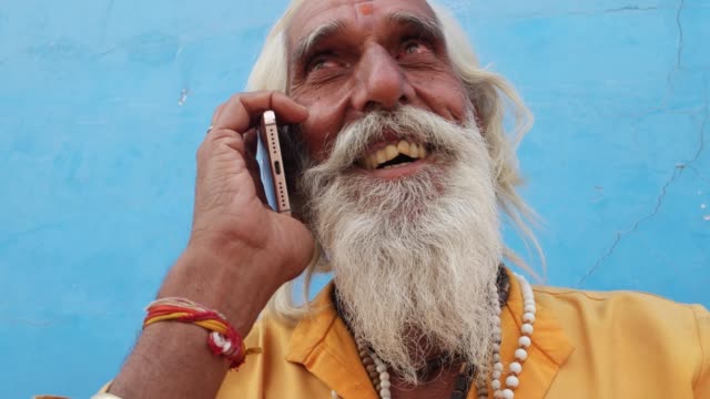 Tilt-up-closeup-of-a-bearded-Hindu-priest-wearing-traditional-saffron-clothes-on-a-call-in-Pushkar,-Rajasthan