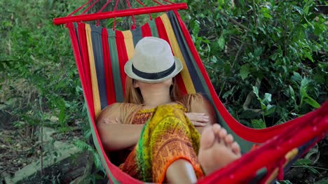 Young-woman-sleeping-in-hammock-with-hat-covering-face