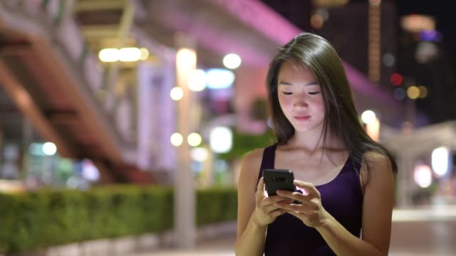 Schöne-asiatische-Frau-draußen-in-der-Nacht-mit-Handy
