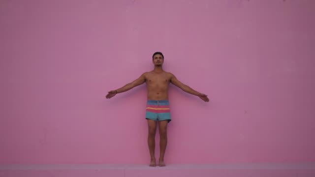 Mixed-race-hispanic-young-man-with-naked-torso-practicing-yoga-fitness-exercise-on-pink-background.-Sport,-meditation-and-lifestyle-concept.-Peaceful-Meditation-for-good-health