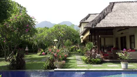 Vista-de-un-jardín-tropical-con-la-piscina-y-las-montañas-sobre-el-fondo-del-cielo-azul-en-un-día-soleado,-Bali,-Indonesia