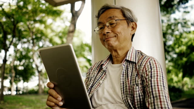 Hombre-mayor-asiático-utilizando-tablet,-sentado-solo-en-el-Banco-en-el-Parque