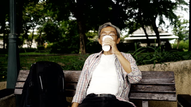 Asiatische-senior-Mann-sitzt-im-Park-einen-Kaffee-und-nutzen-Smartphone