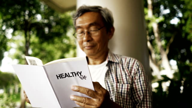 Asian-senior-man-reading-Healthy-Life-book-alone-in-the-park