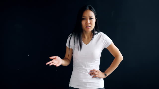 Portrait-of-angry-Asian-woman-talking-and-gesturing-expressing-negative-emotions-standing-against-black-background.-Young-people,-negativity-and-anger-concept.