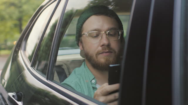 Stilvolle-junge-Mann-fahren-in-einem-Auto-sitzen-auf-dem-Beifahrer-Sitz-nutzt-Smartphone-Typen-Nachricht,-blättert-durch-Internet.-Kamera-Schuss-von-außerhalb-des-Fahrzeugs.