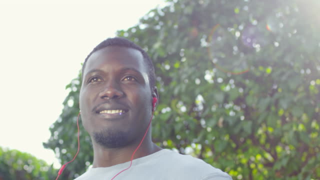 Afrikanische-Sportler-mit-Kopfhörern-lächelnd-in-die-Kamera-im-freien