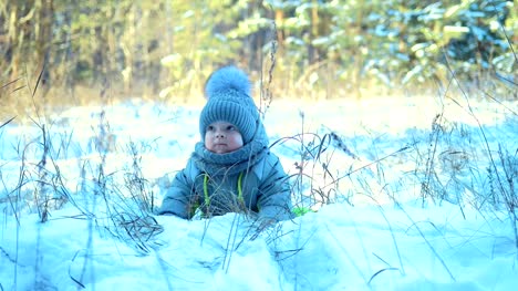 Happy-baby-lying-in-a-snowdrift.-Kid-gets-up-from-a-snowdrift.-Baby-looks-and-smiles
