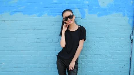 Young-beautiful-asian-girl-wearing-sunglasses-and-smiling-posing-near-wall-outdo