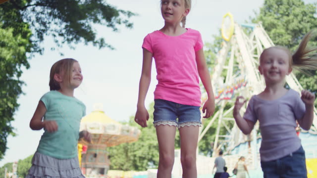 Three-little-girls-at-a-fair-hop-up-and-down-with-excitement-and-hug-each-other