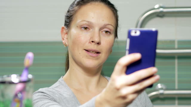 Junge-attraktive-Frau-Selfie-Telefon-im-Bad-des-Hotelzimmers-zu-tun.-Sie-lächelt-und-ändert-die-Haltung-für-ein-besseres-Foto