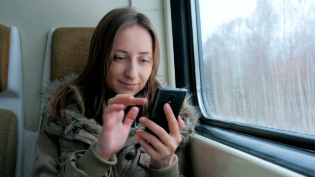 Pensive-woman-traveling-on-a-train-and-using-a-smartphone
