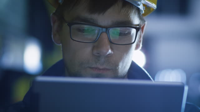 Technician-in-Glasses-and-Hard-Hat-Using-Tablet-in-Industrial-Environment.-Reflections-of-Screen-Glasses