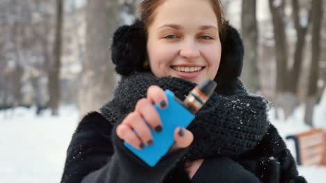 Linda-mujer-sostiene-el-cigarrillo-electrónico-en-el-parque-de-invierno