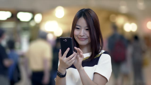 Hübsche-Chinesin-SMS-und-im-Gespräch-mit-dem-Telefon-im-öffentlichen-Raum.-Glücklich-zu-sein,-Lächeln-und-Spaß-haben.